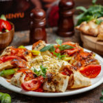 beyti wrapped kebab topped with tomato sauce, served with tomato, pepper, yoghurt